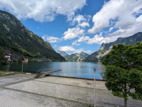 Scenery at Ebensee. A lake surrounded by towering mountains on all sides beneath a lightly clouded sky. There's a quay with concrete springboard, but no people populating it.
